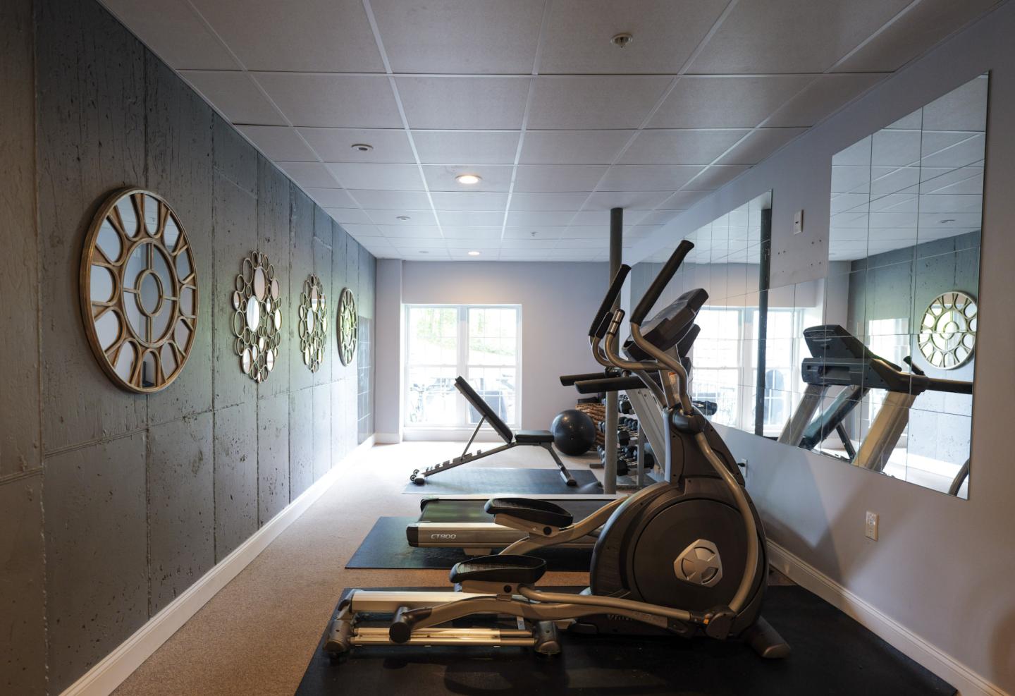 Small gym with exercise machines, large mirrors, and circular wall decorations.