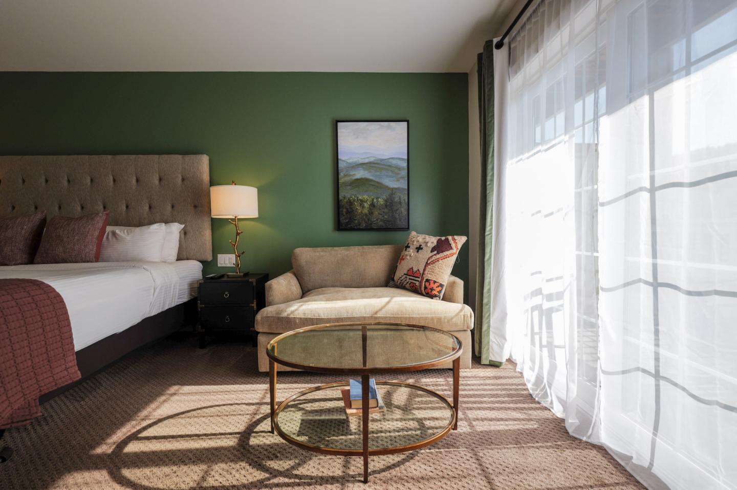 Cozy hotel room with a bed, sofa, and glass table by a window.