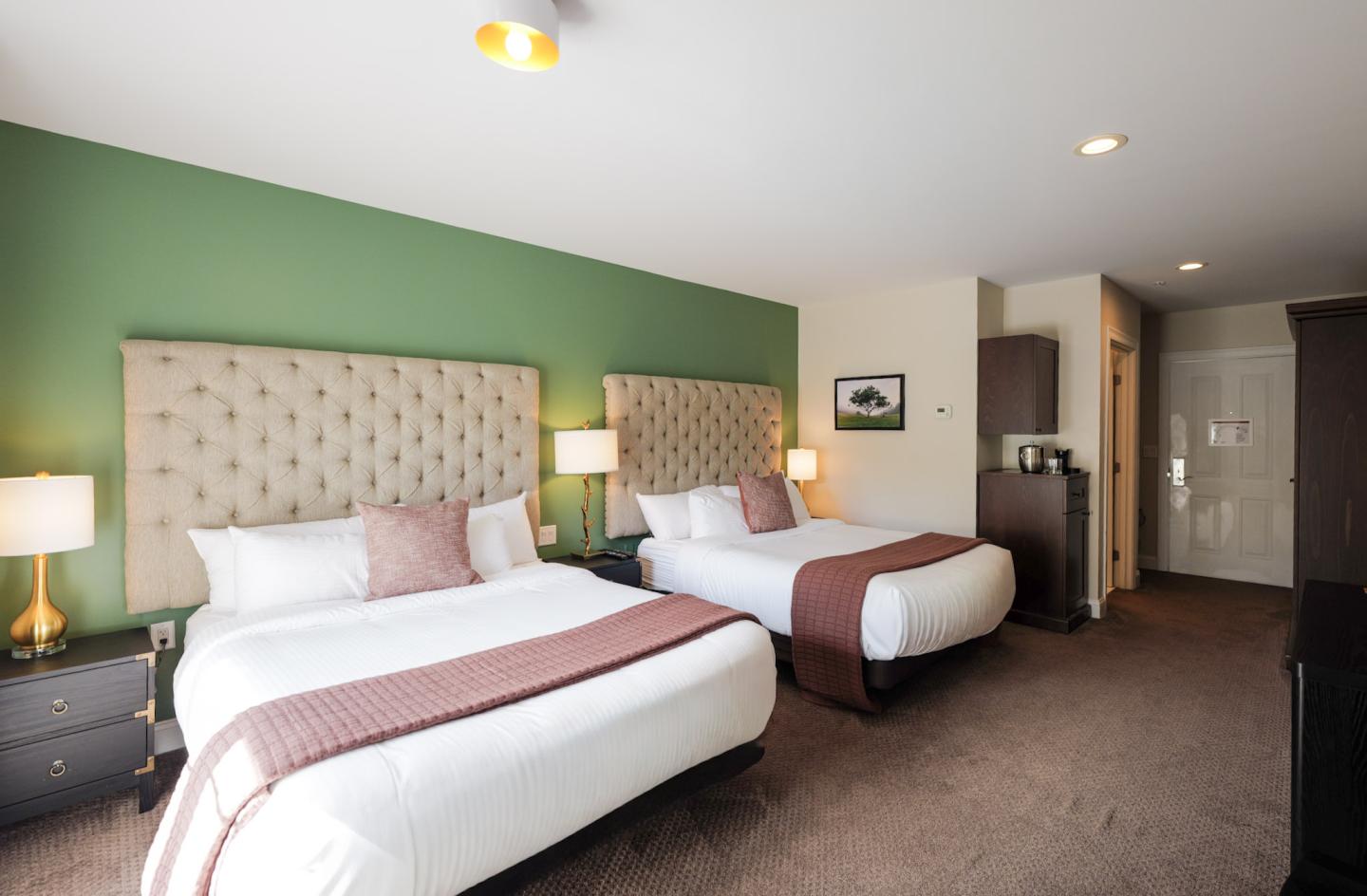 Two double beds in a hotel room with green accent wall and warm lighting.