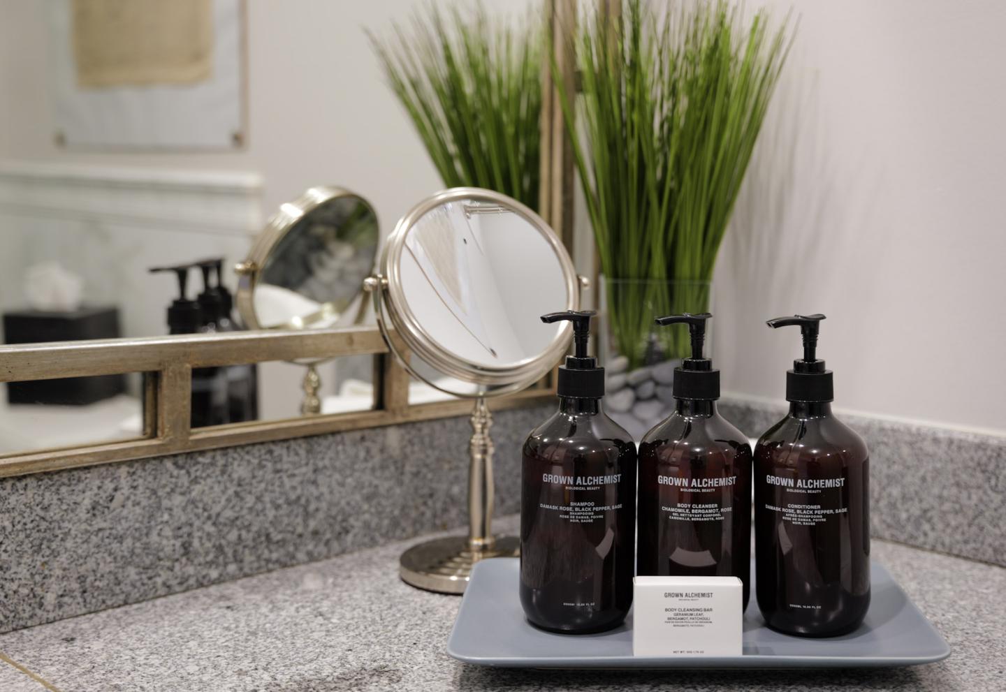 Three brown lotion bottles on a tray beside a mirror and green plant.