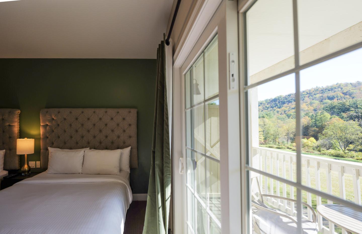 Sunny room with a bed, green walls, and balcony view of trees.