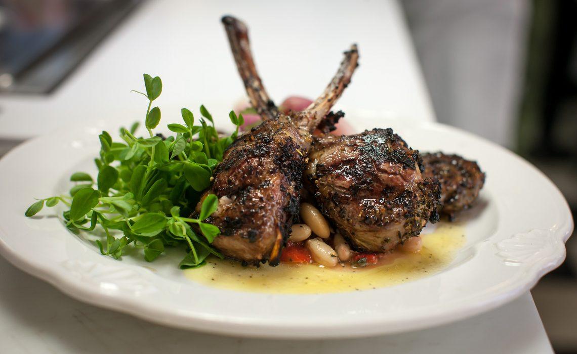 Grilled lamb chops with greens and beans on a white plate.