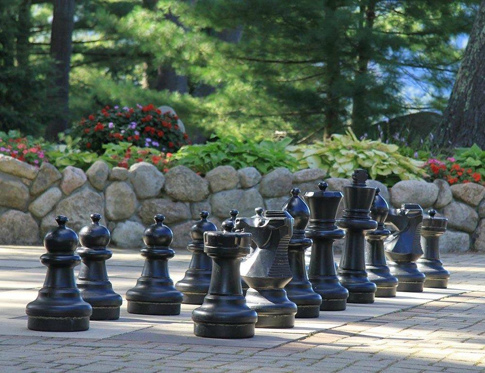 Giant black chess pieces on a stone patio, lush garden in the background.