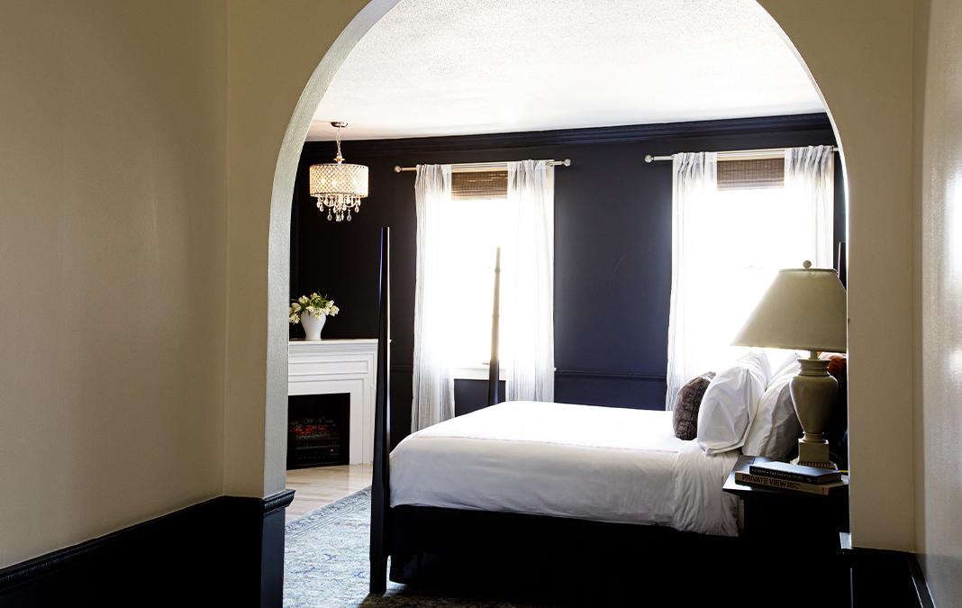 Cozy bedroom with dark walls, white bed, and arched entryway.