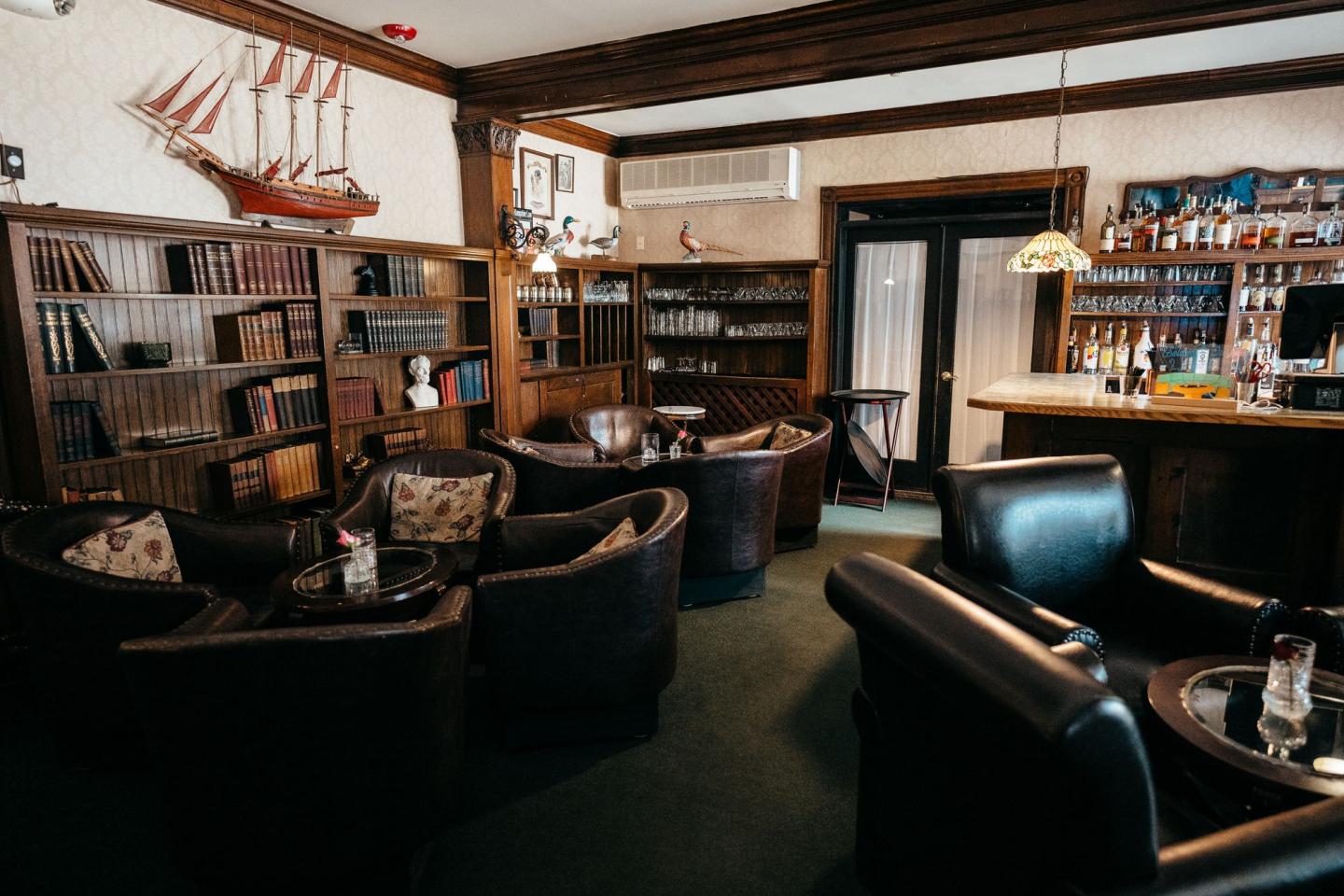 Cozy bar with leather chairs, wooden shelves, and dim lighting.
