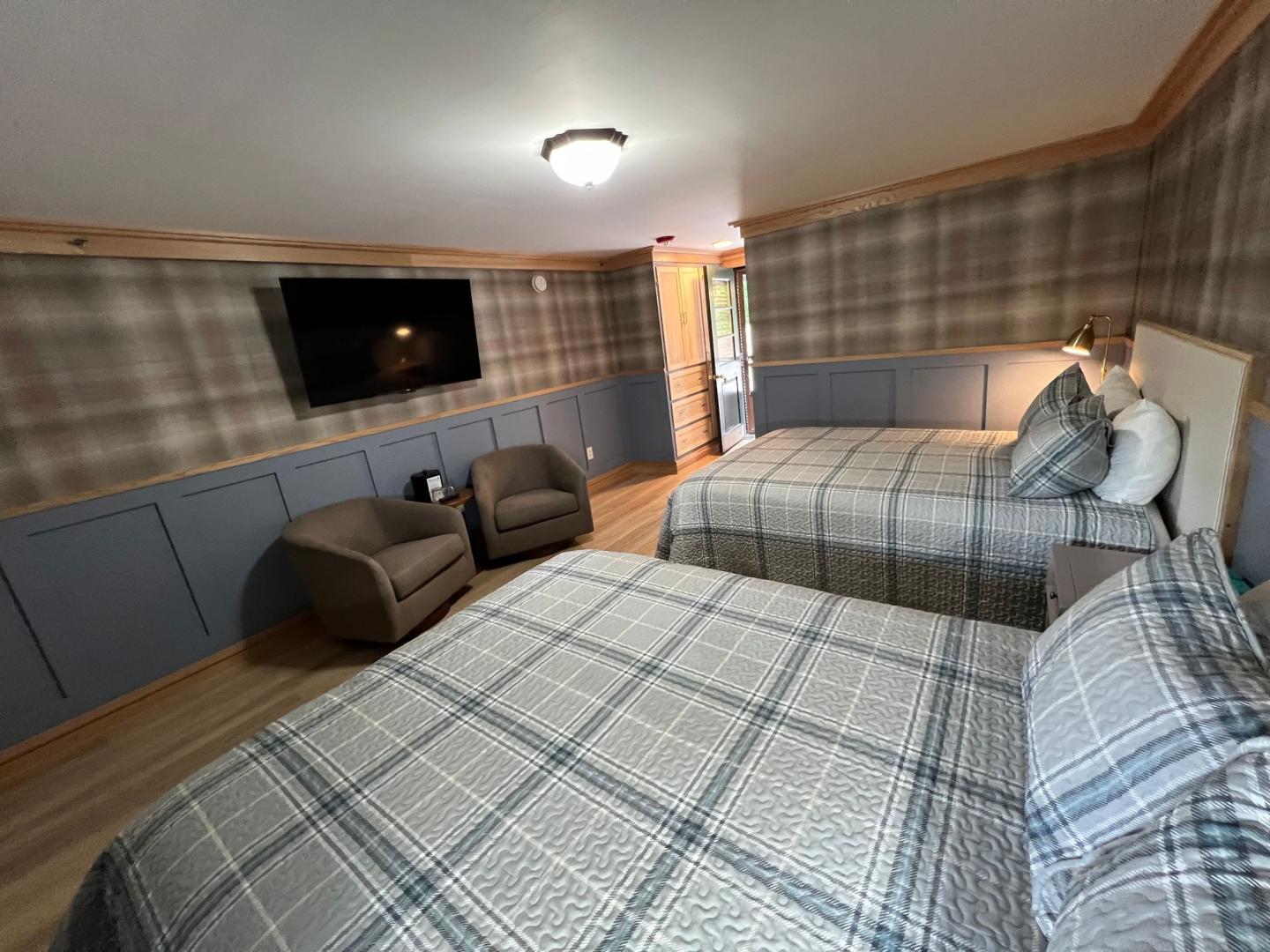 Two beds in a plaid-themed room with two chairs and a wall-mounted TV.