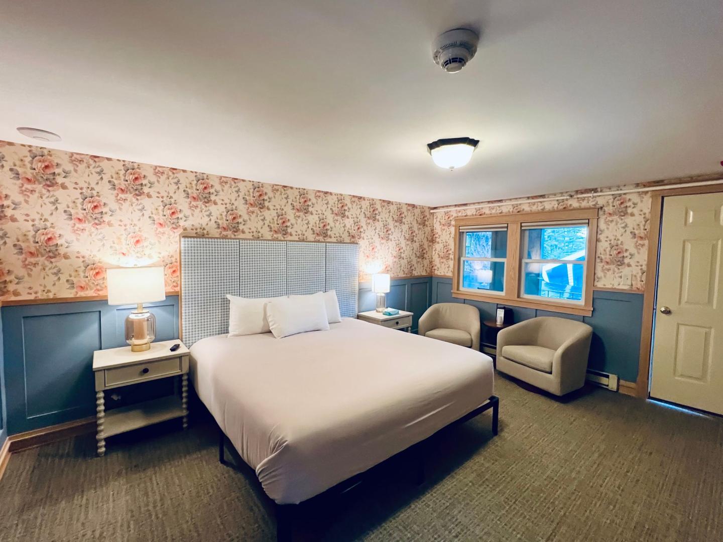 Cozy bedroom with floral wallpaper, king bed, and seating area.