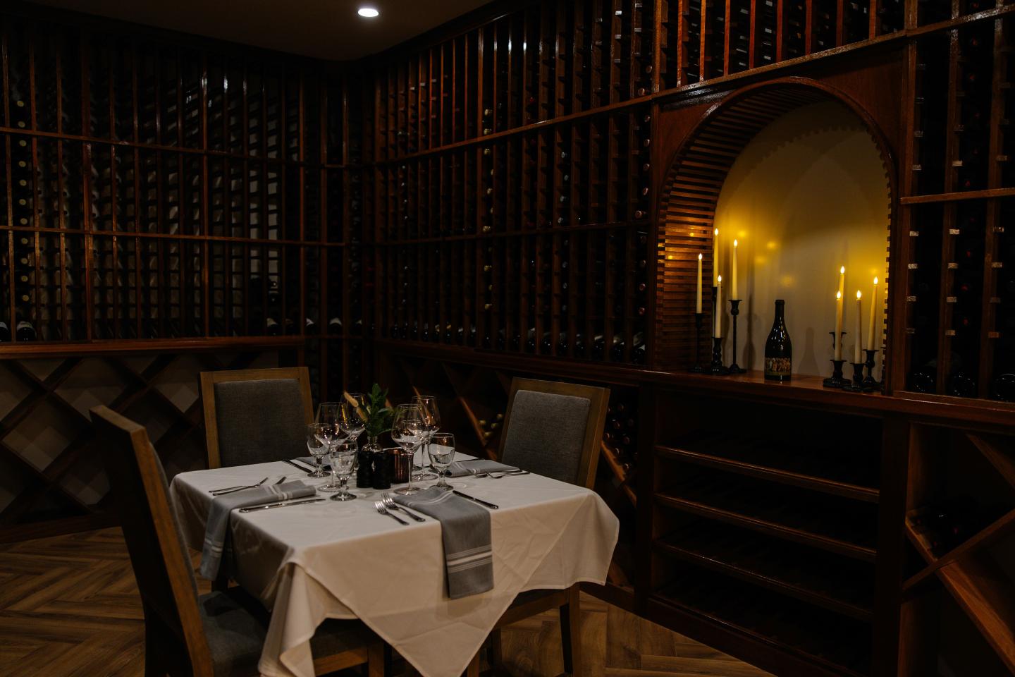 Dimly lit wine cellar dining table with candles and elegant place settings.