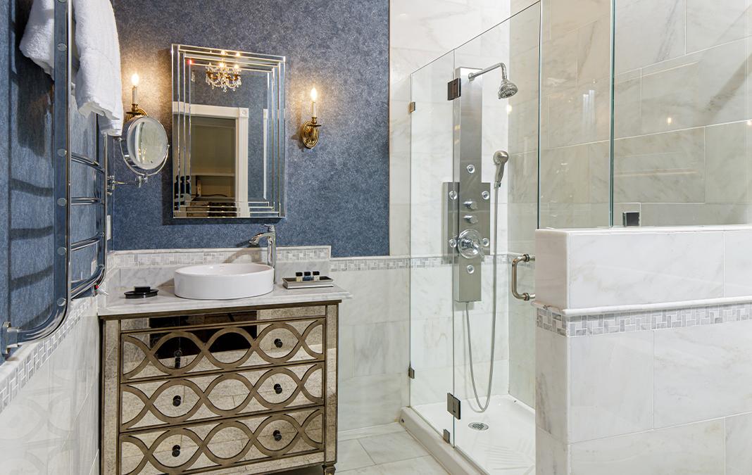 Elegant bathroom with glass shower, ornate vanity, and blue textured walls.