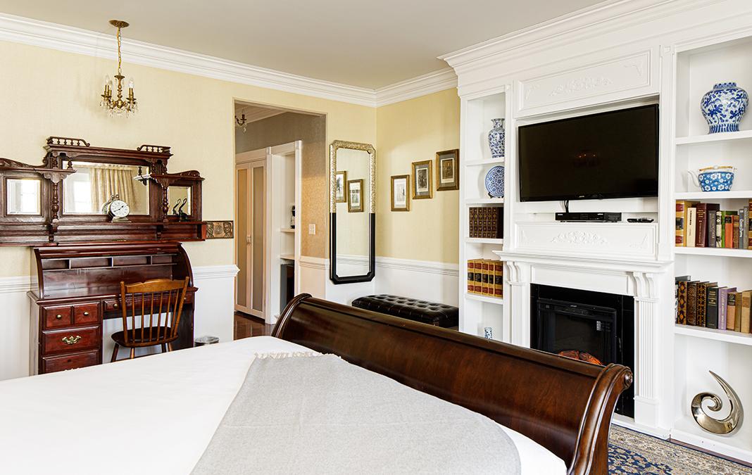 Warm bedroom with wooden furniture, a fireplace, and a mounted TV.