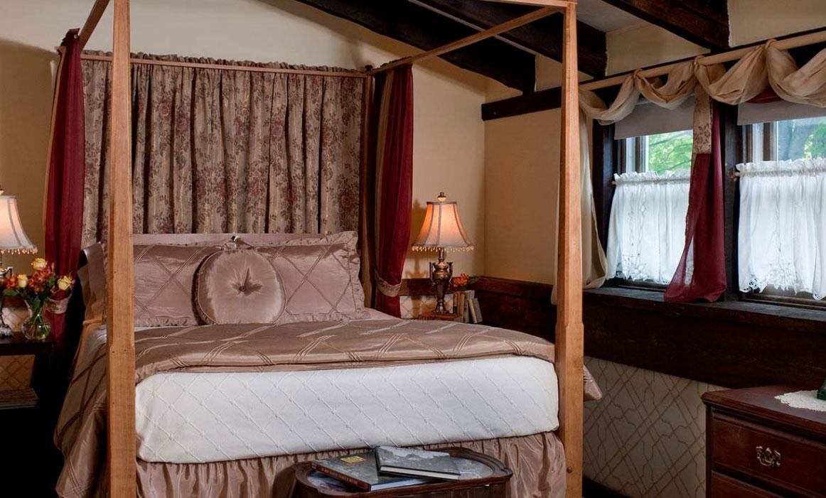 Cozy bedroom with a four-poster bed and two lamps beside curtained windows.