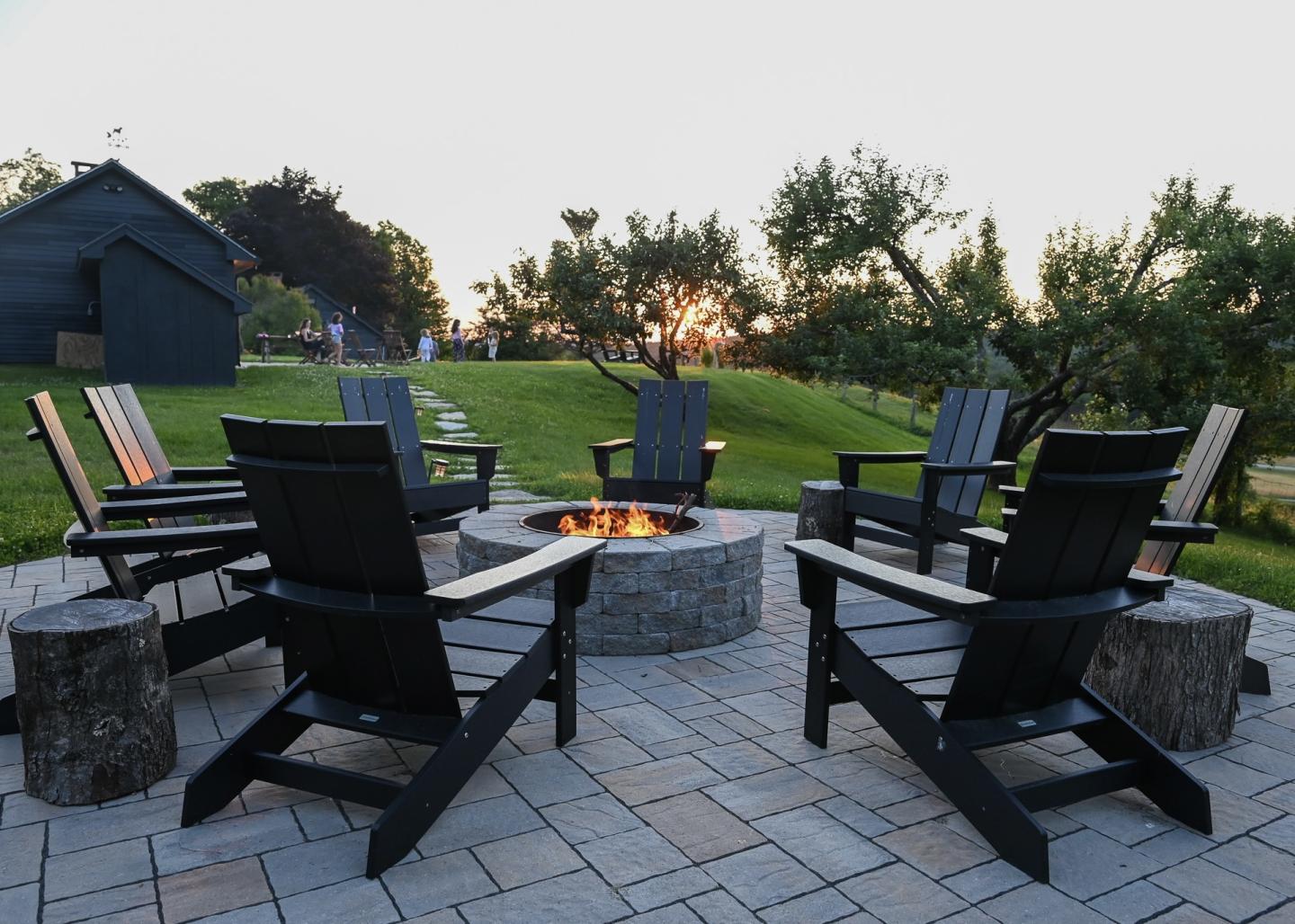Fire pit surrounded by black chairs on a patio at sunset.