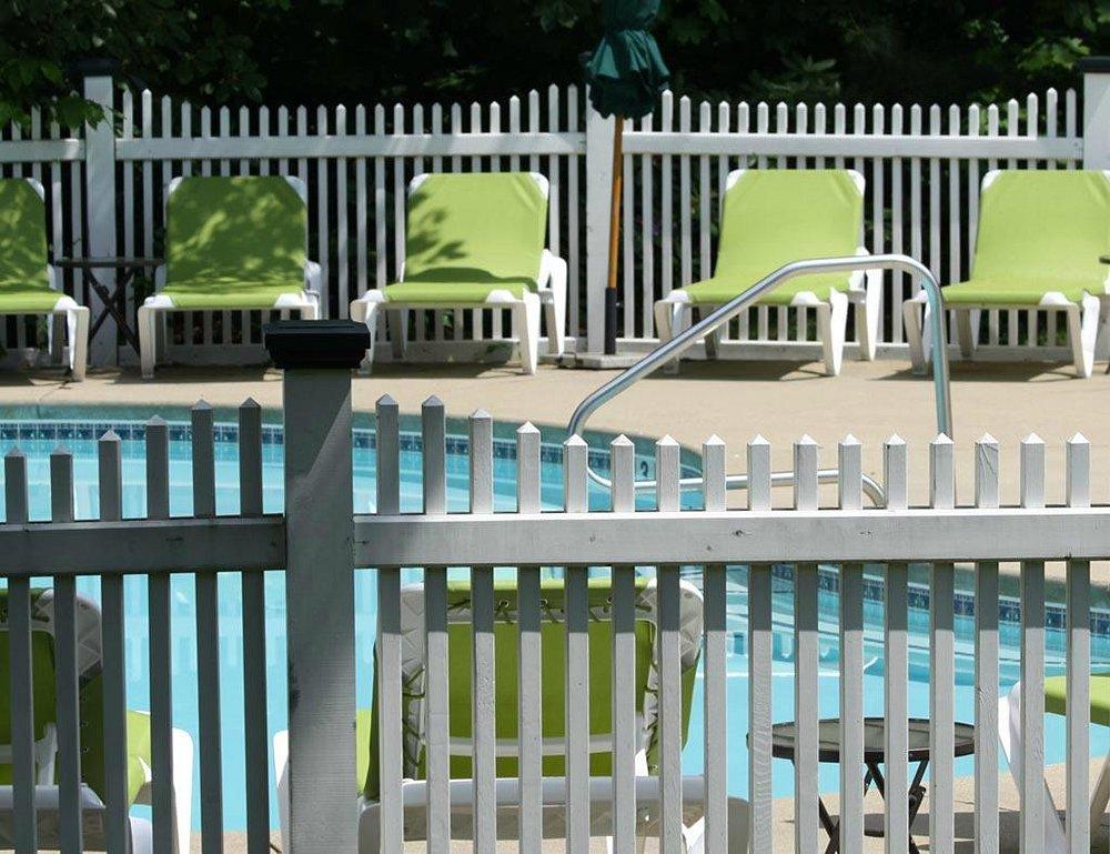 Pool with green lounge chairs and white fence in sunlight.
