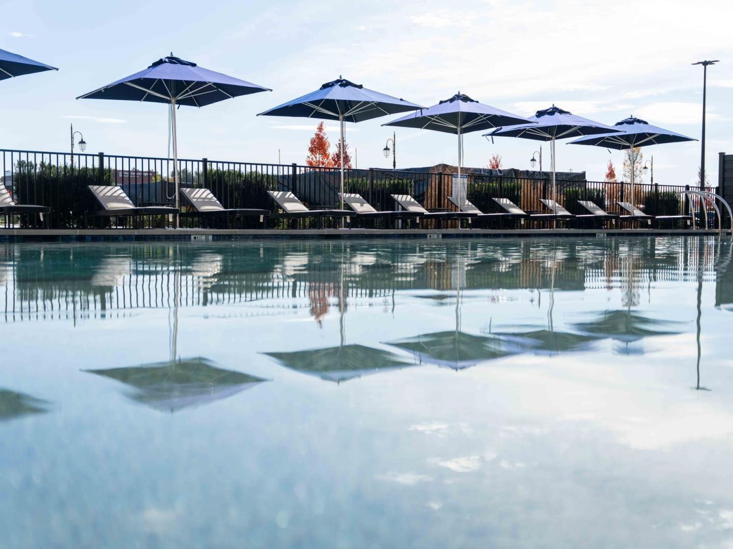 Poolside with sun loungers and blue umbrellas reflecting on water.