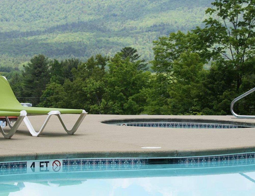 Poolside with a green lounge chair, trees, and mountains in the background.