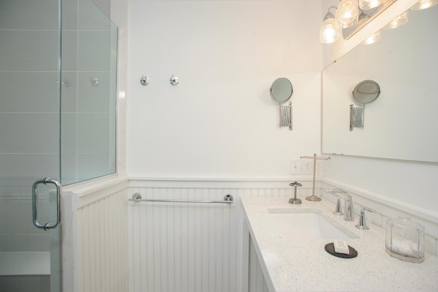 Modern bathroom with white countertops, glass shower, and bright lighting.