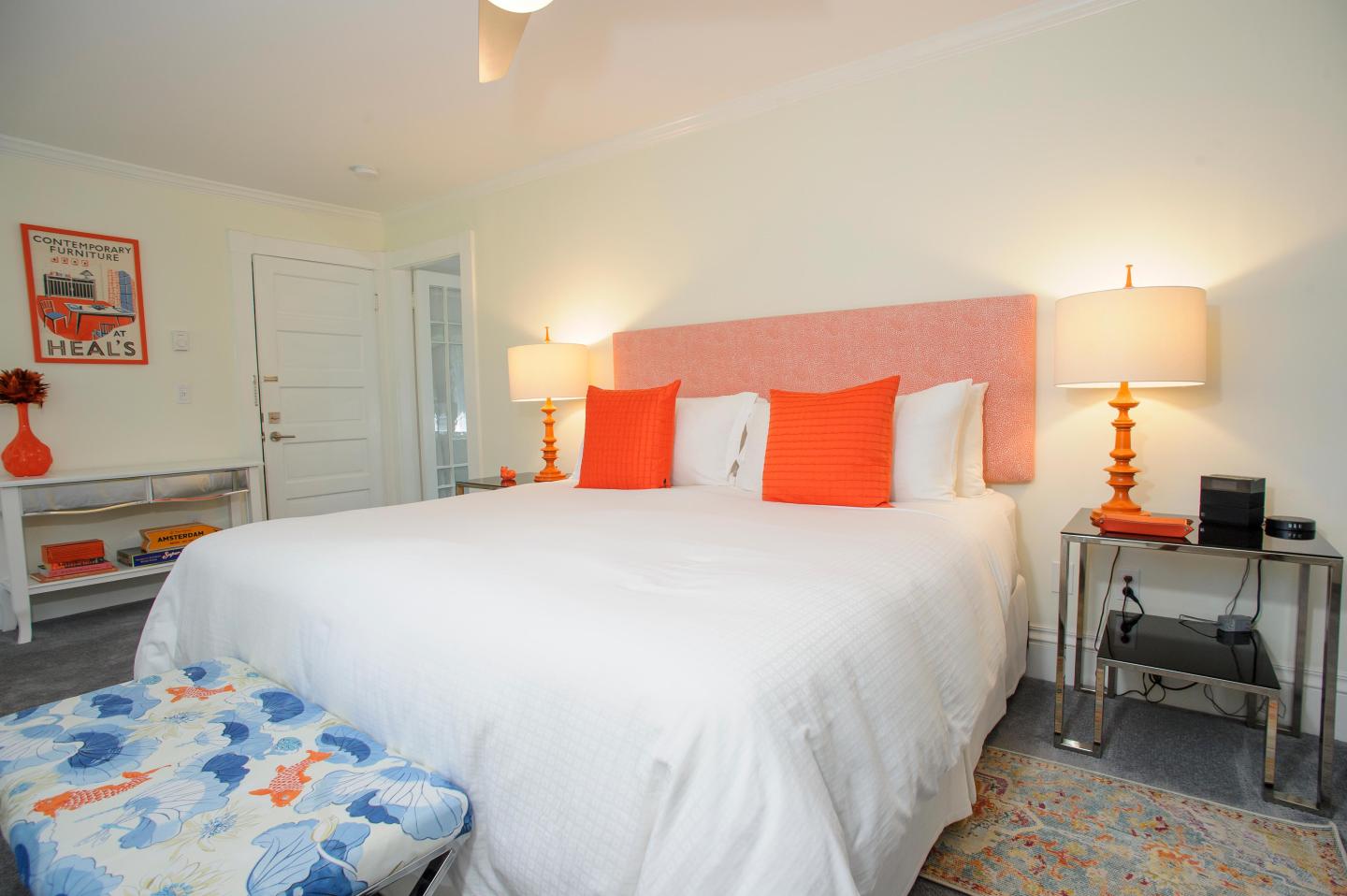 Bedroom with white bed, orange pillows, and warm lighting.