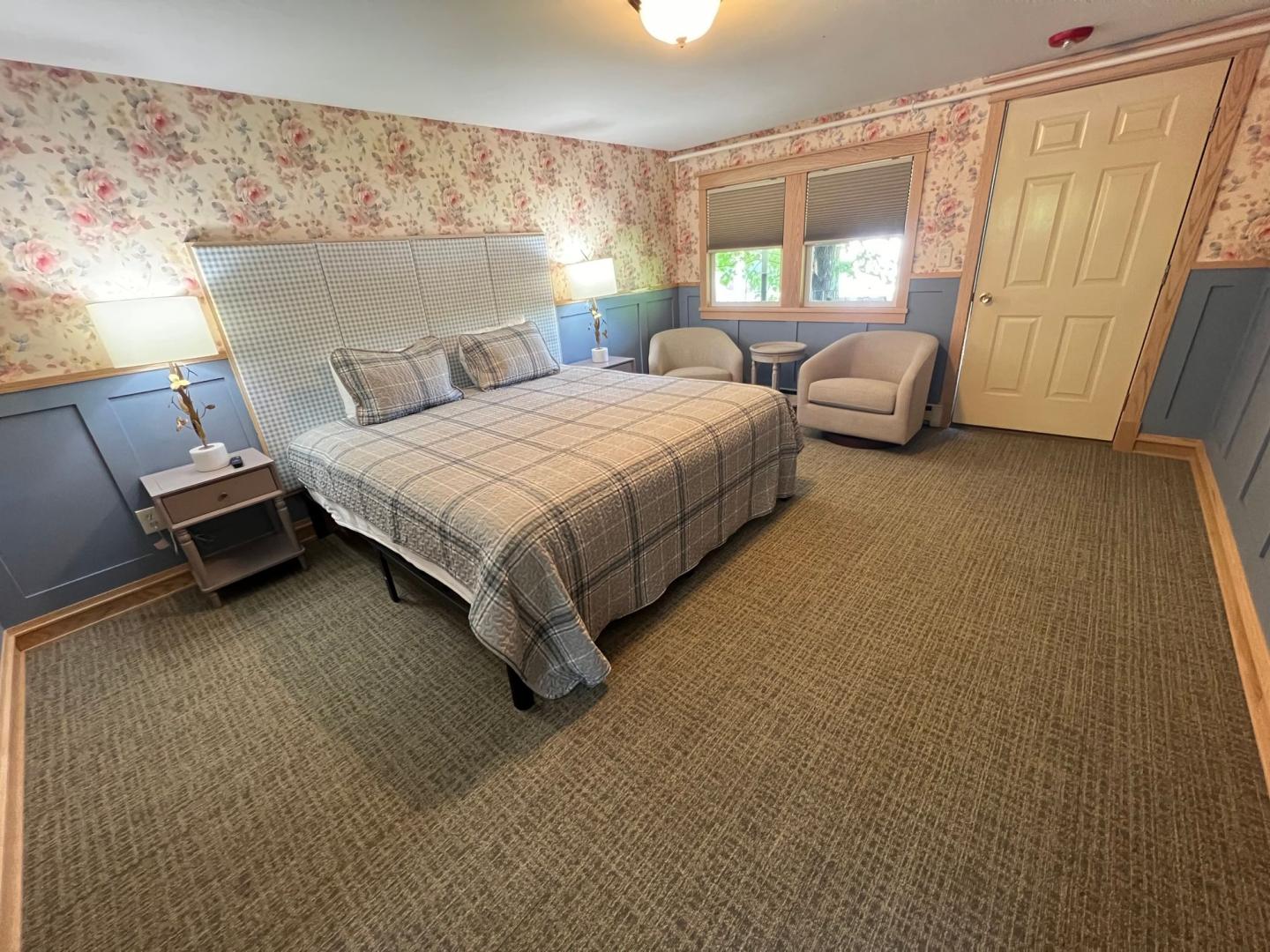 Bedroom with plaid bedding, floral wallpaper, and two armchairs.