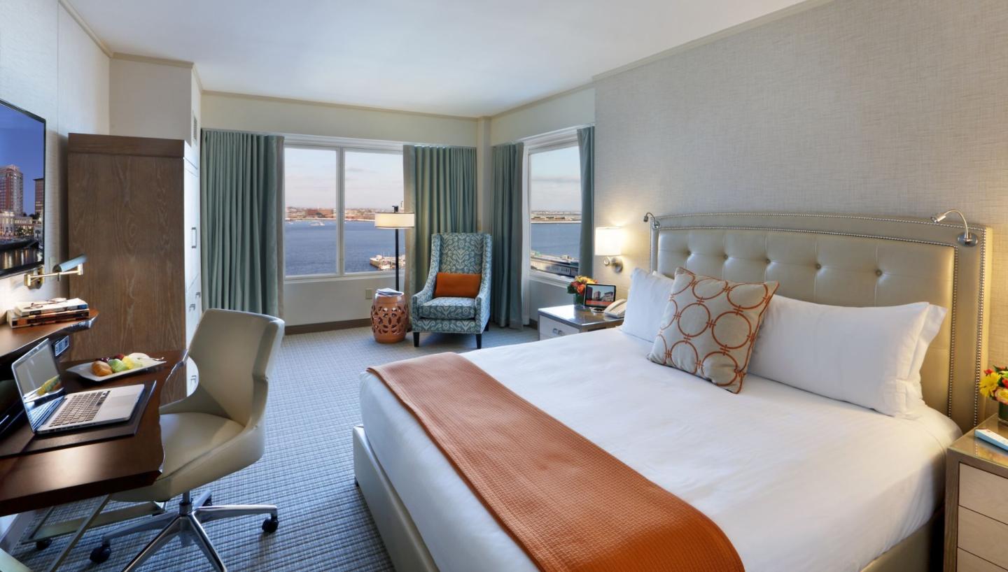 Hotel room with a king bed, desk, and ocean view through large window.