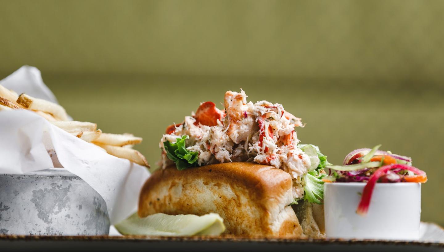 Lobster roll with fries and slaw on a plate.