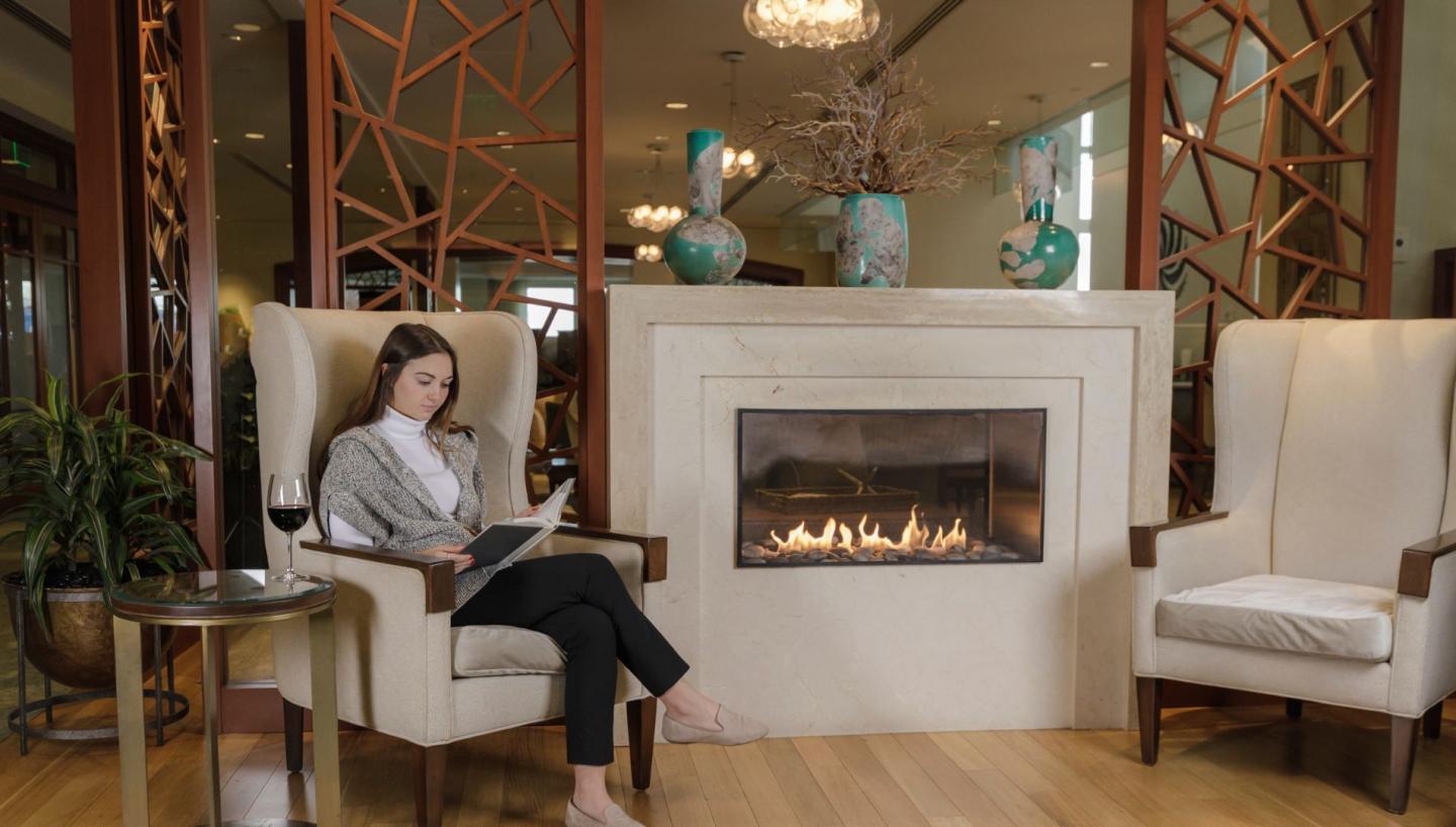 Woman reading by a cozy indoor fireplace in an elegant setting.