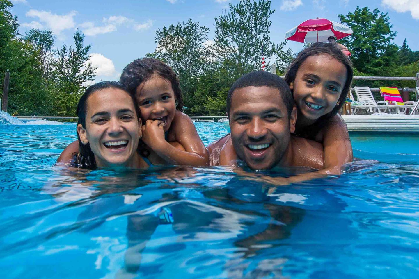 Family smiling in a pool on a sunny day.