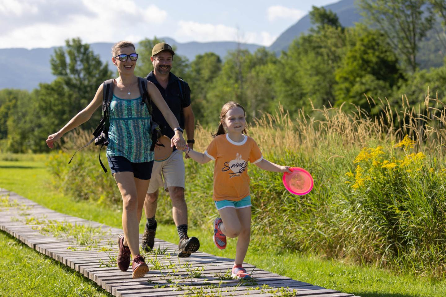 Family holding hands, walking on a path in a sunny, green park.