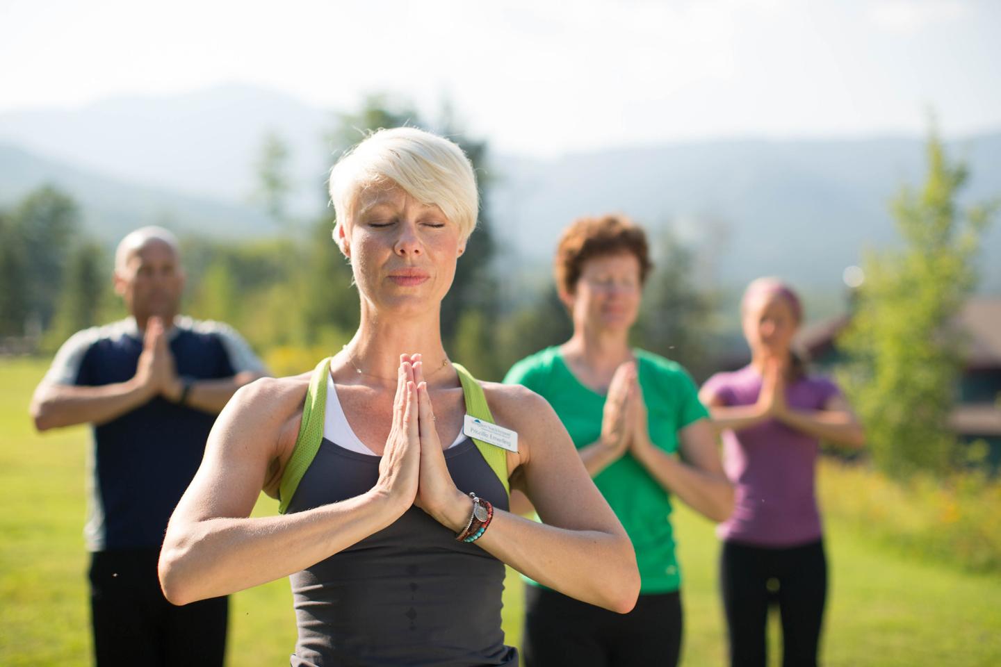 Group practicing yoga outdoors, mountains in the background.