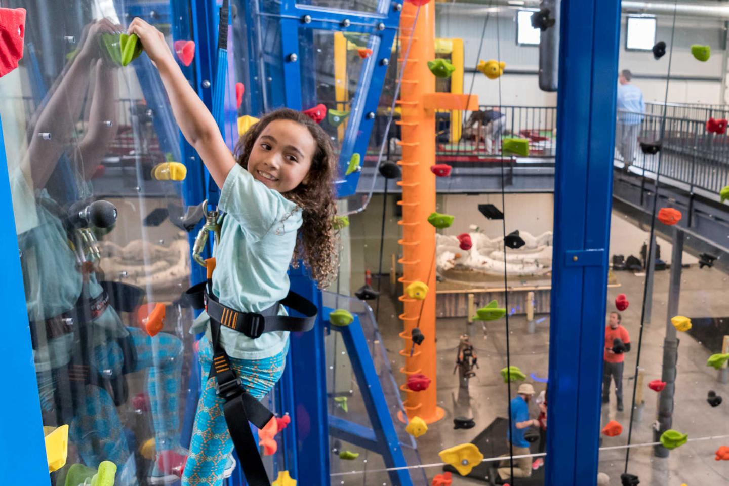Child smiling while climbing a vibrant indoor rock wall.
