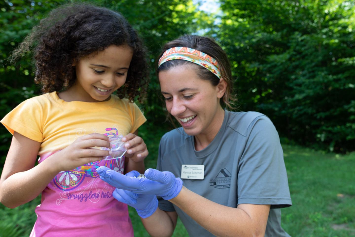 Child and woman smiling at a small creature held in the woman's gloved hands.