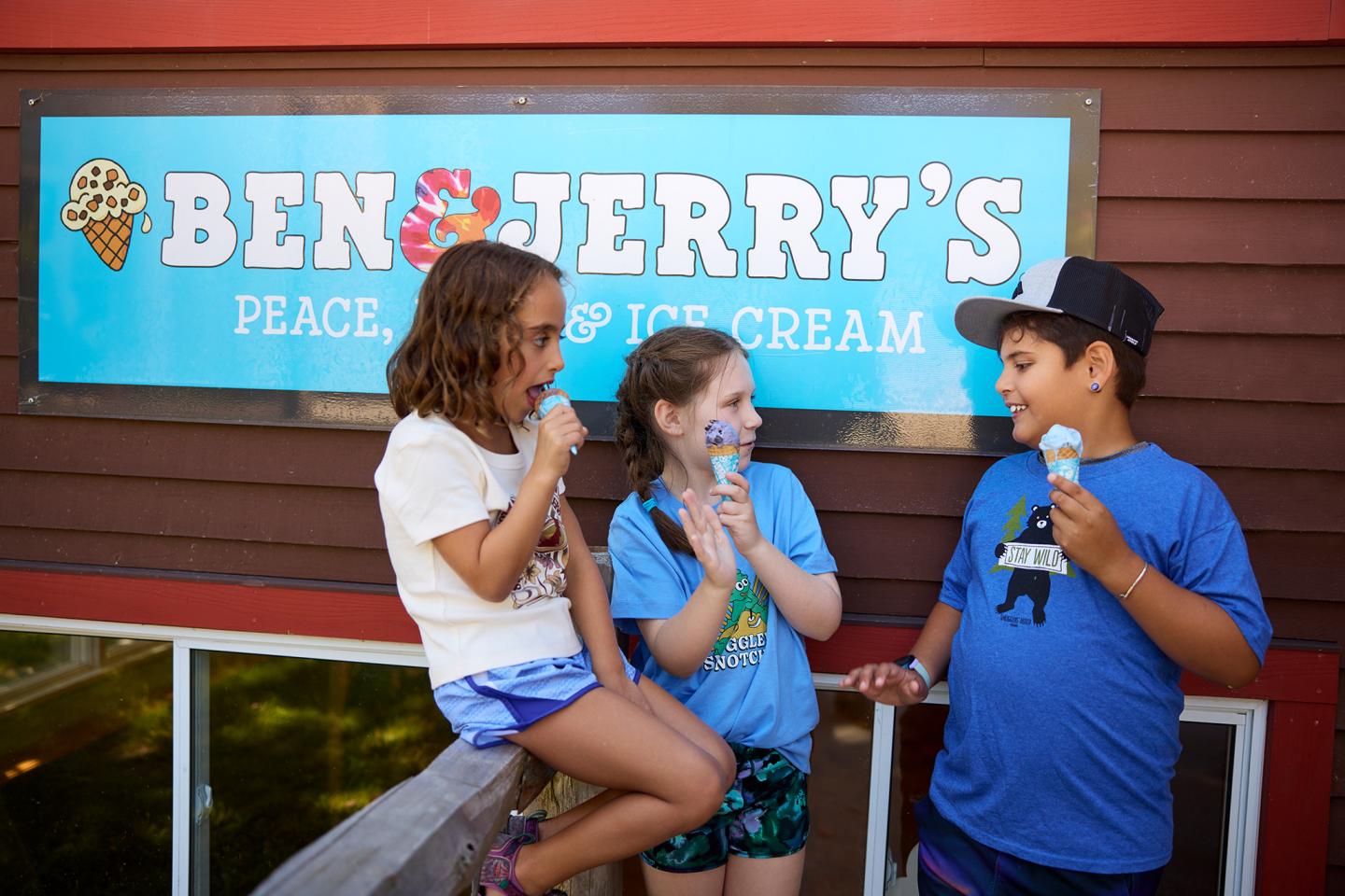Three kids enjoying ice cream in front of a Ben &amp; Jerry's sign.