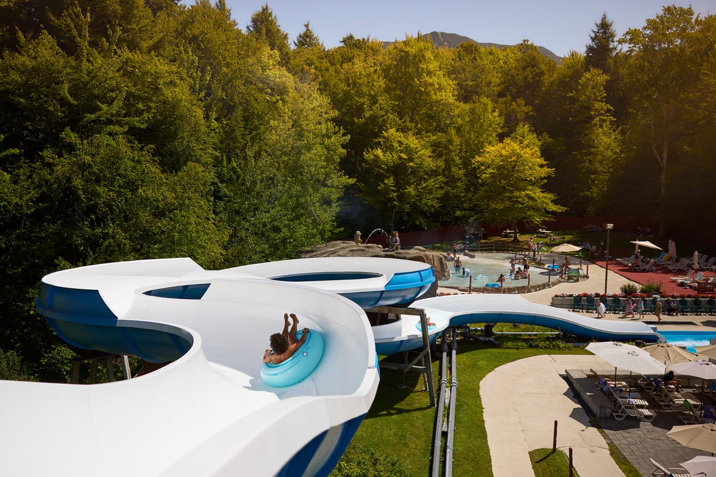Person sliding down a white water slide in a leafy park.