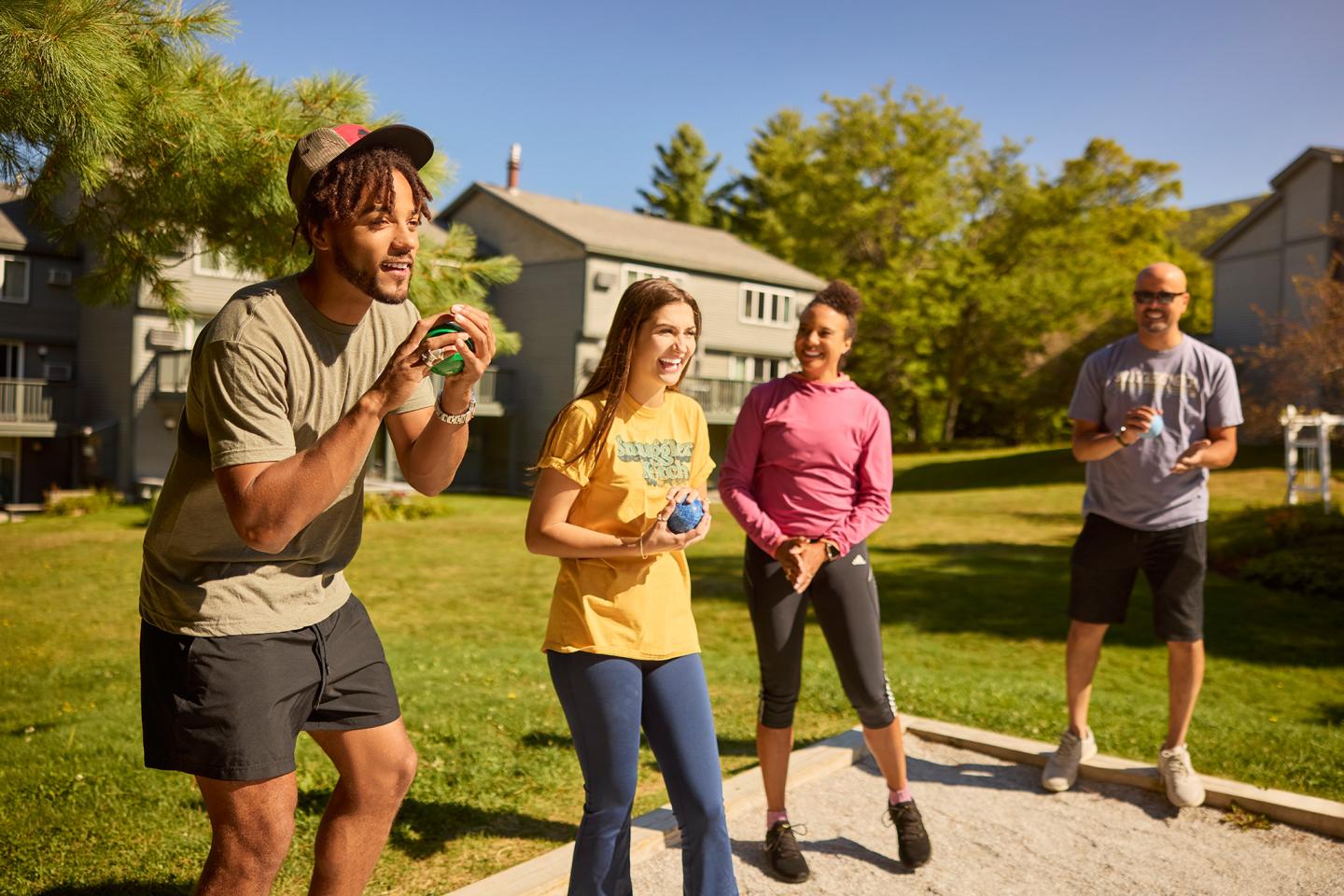 Friends playing bocce ball on a sunny day in a grassy yard.