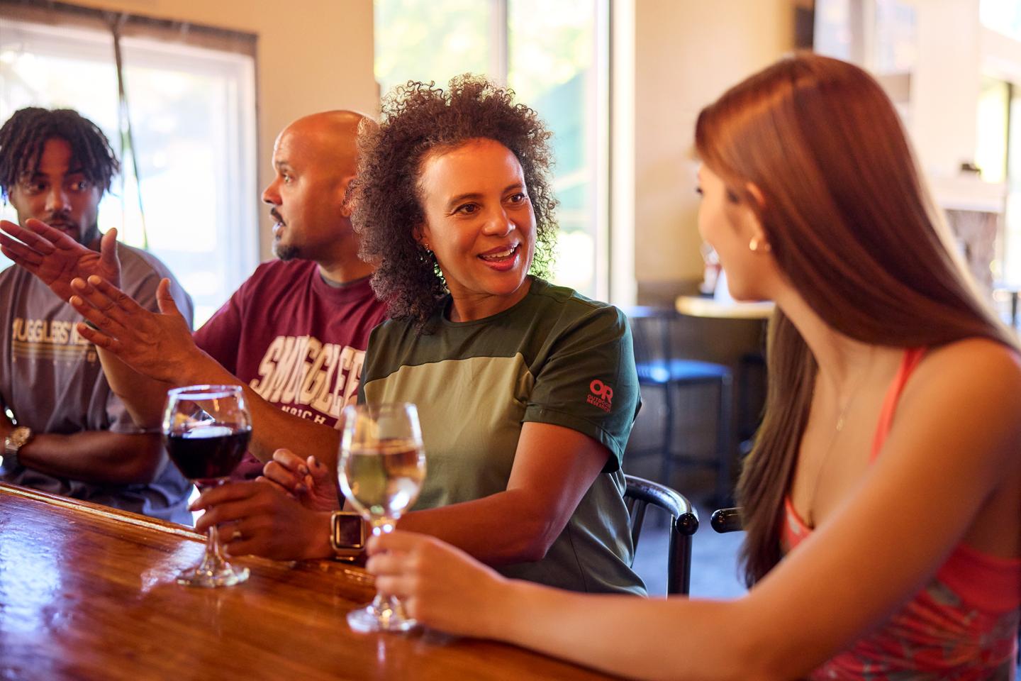 Group of people enjoying drinks at a wooden bar, conversing and smiling.