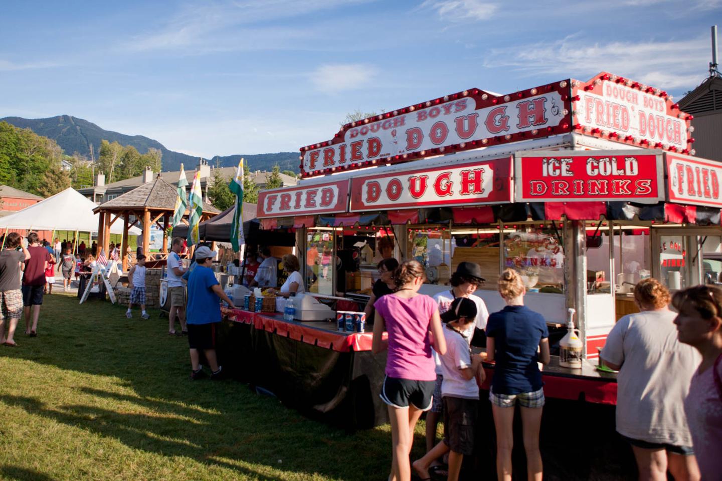 Fried dough stand at an outdoor fair with people in line.