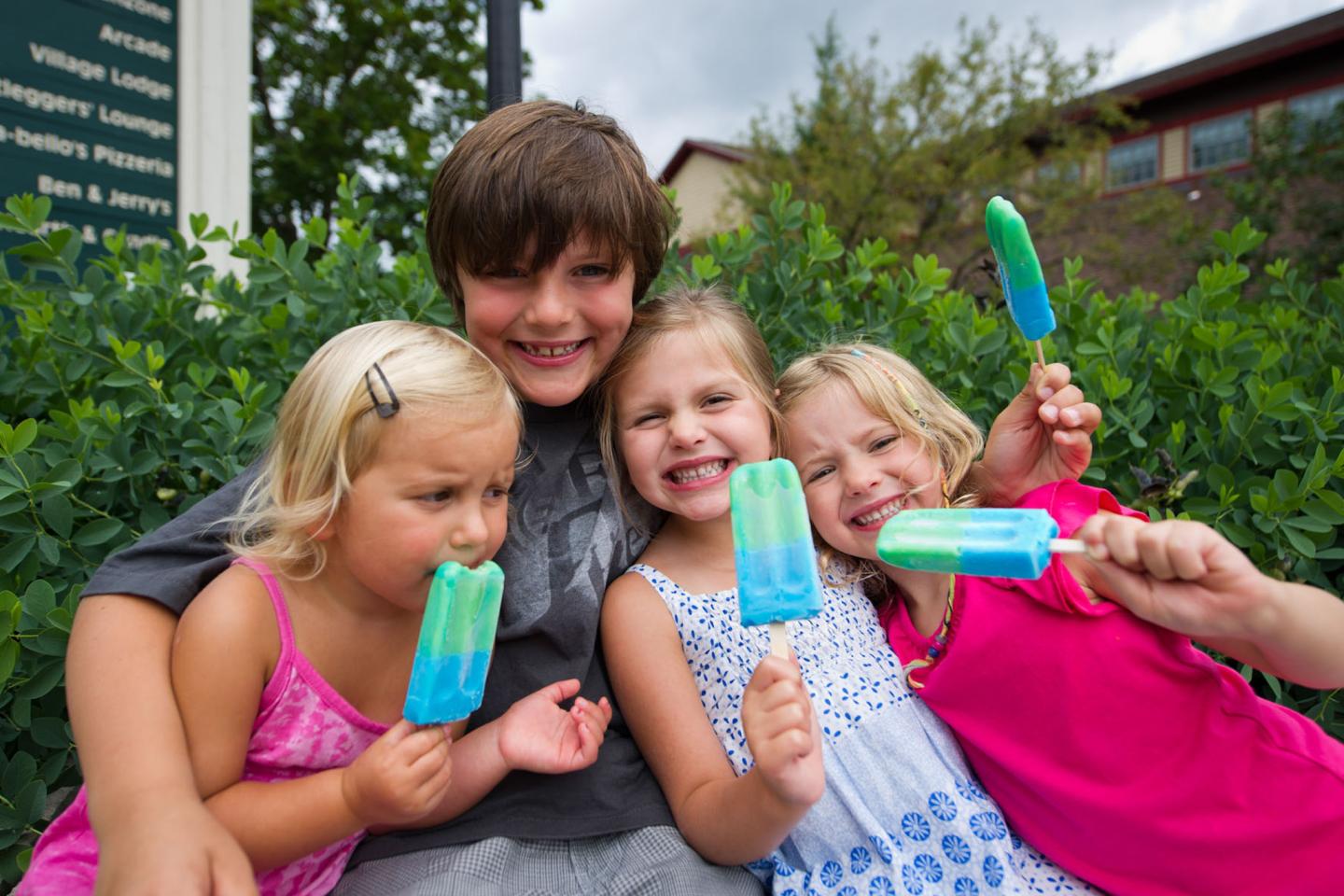 Four children eating colorful popsicles, smiling outdoors.