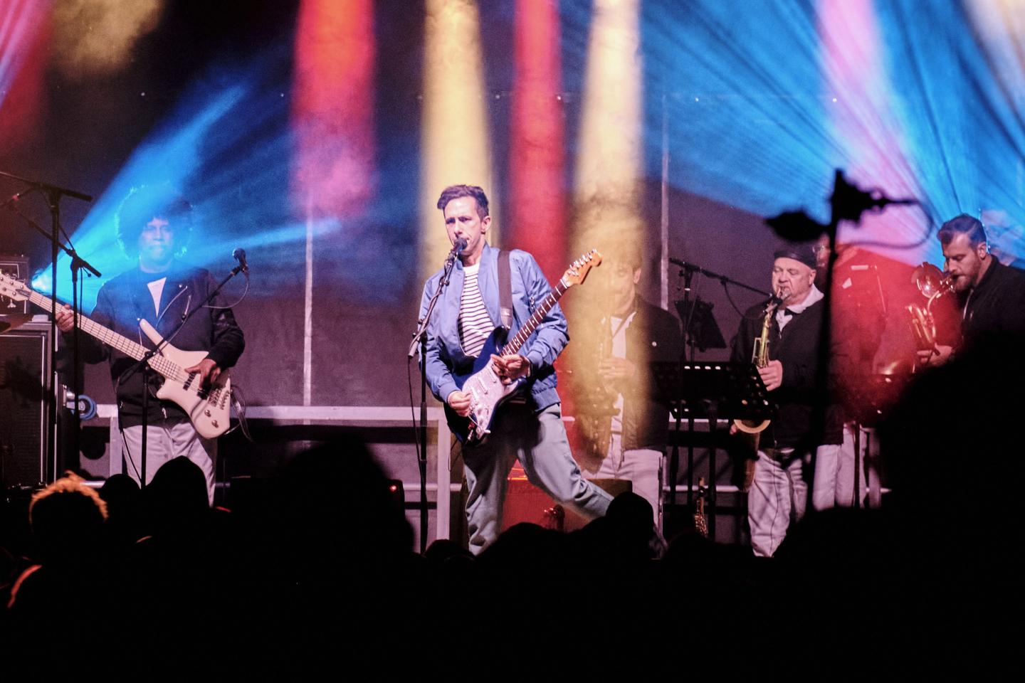 Band performing on stage with colorful lights in background.