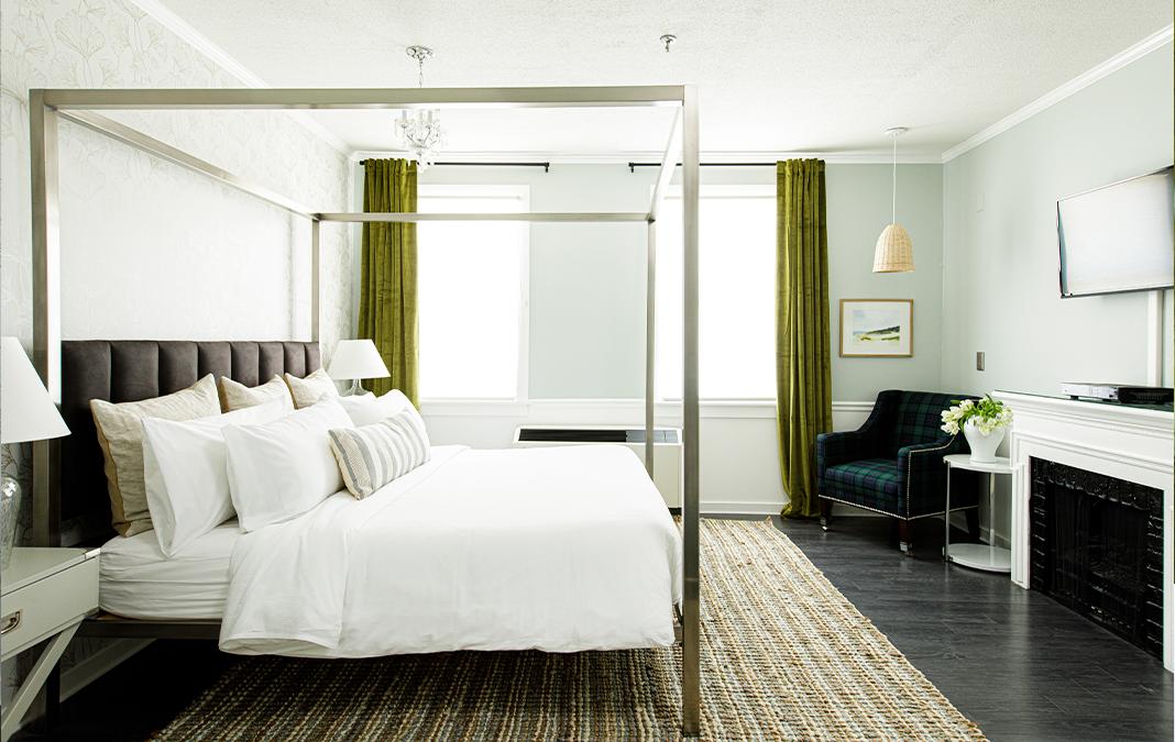 Spacious bedroom with a canopy bed, green curtains, and a fireplace on the right.