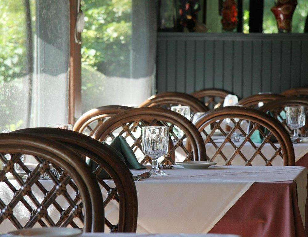 Elegant restaurant with set tables, wooden chairs, and natural light.