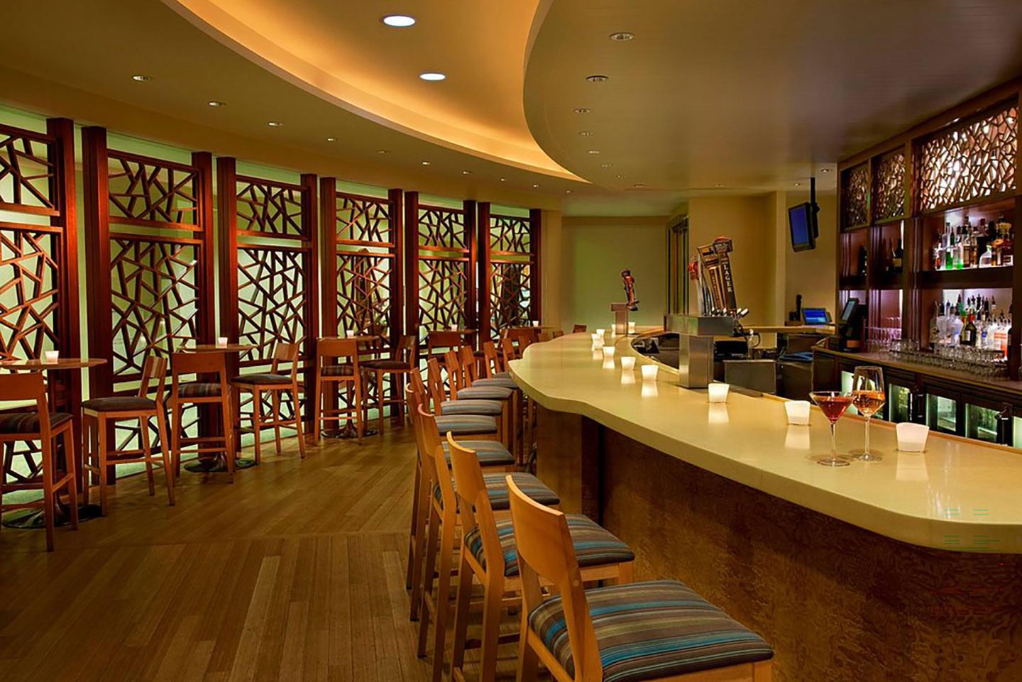 Cozy, dimly lit bar with wooden stools and patterned walls.