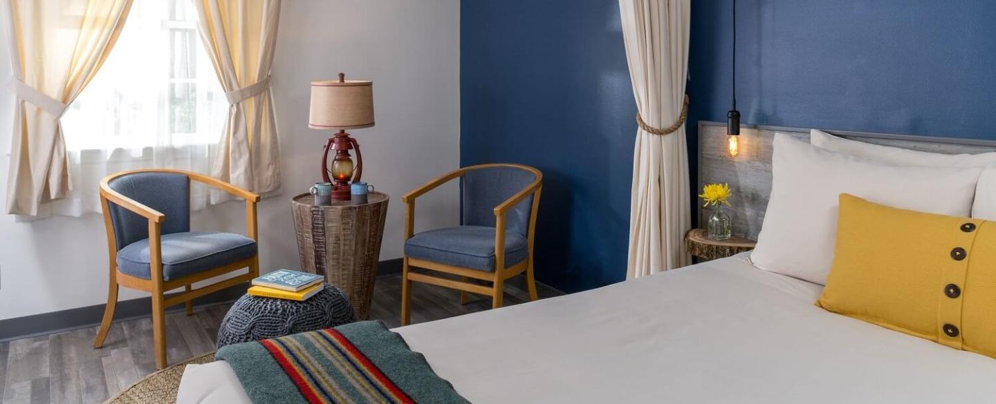 Cozy bedroom with blue walls, yellow accents, two chairs, and a window.