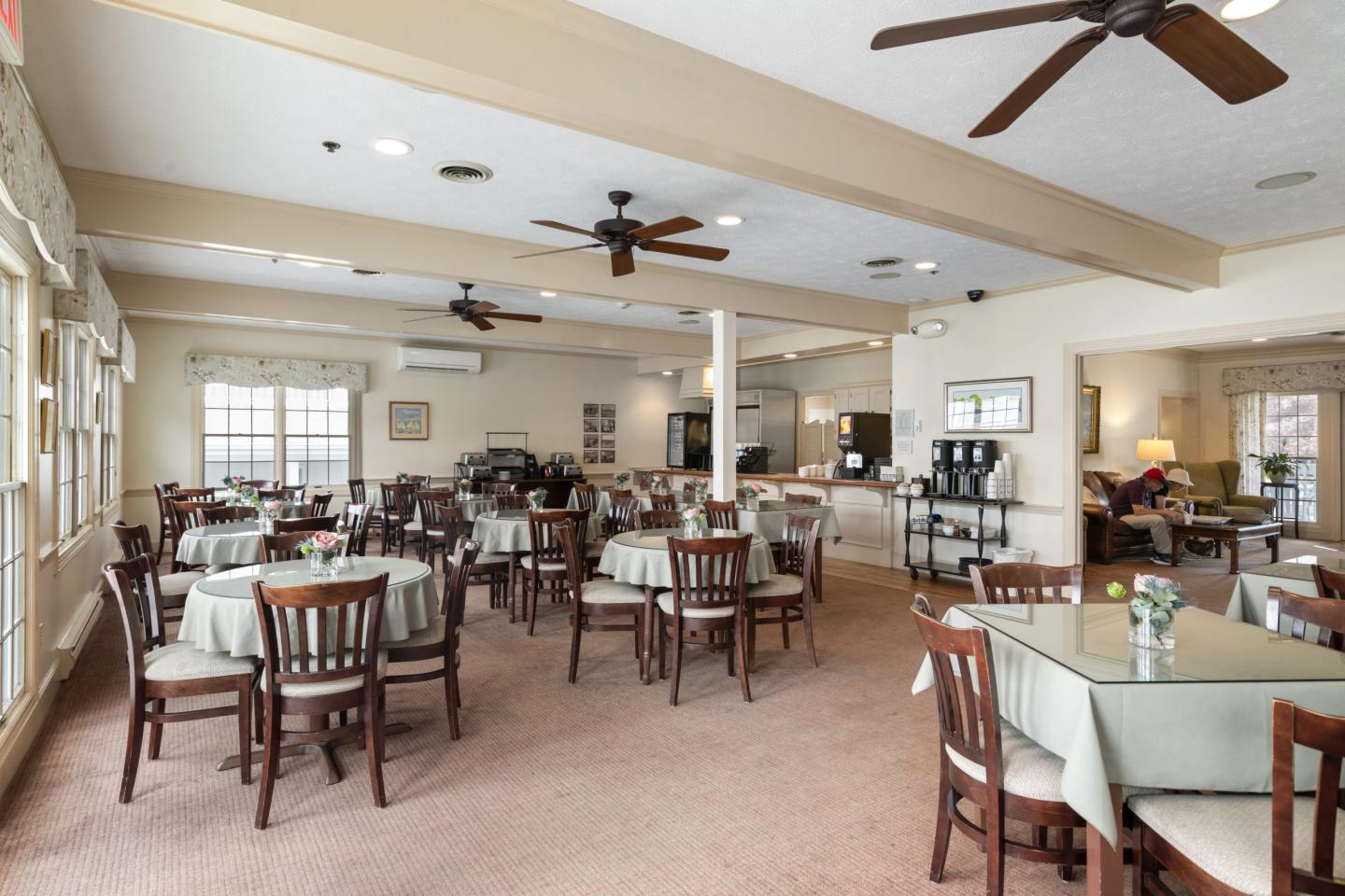 Spacious dining room with round tables and chairs, neutral tones, ceiling fans.