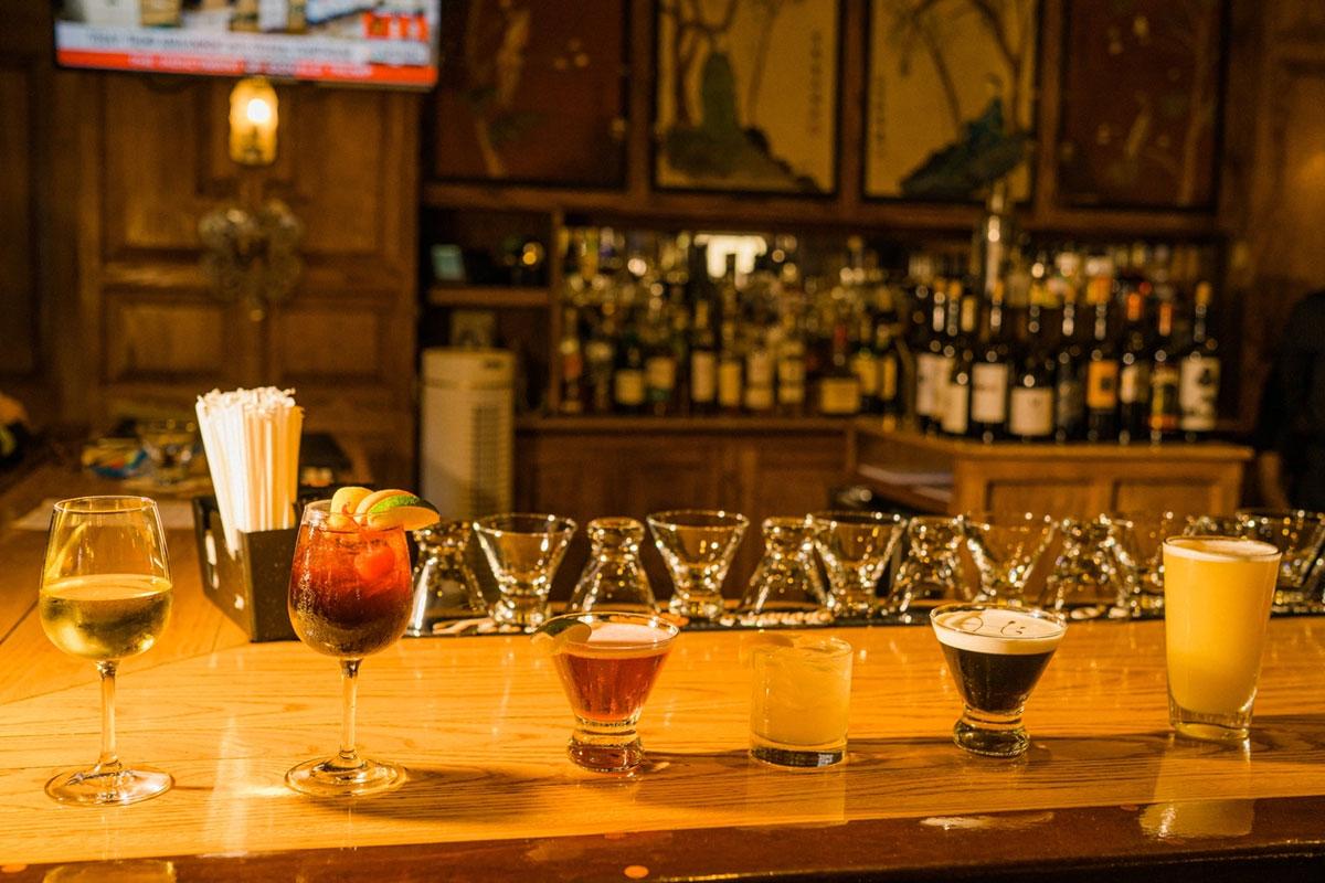 A row of colorful drinks on a dimly lit bar counter.