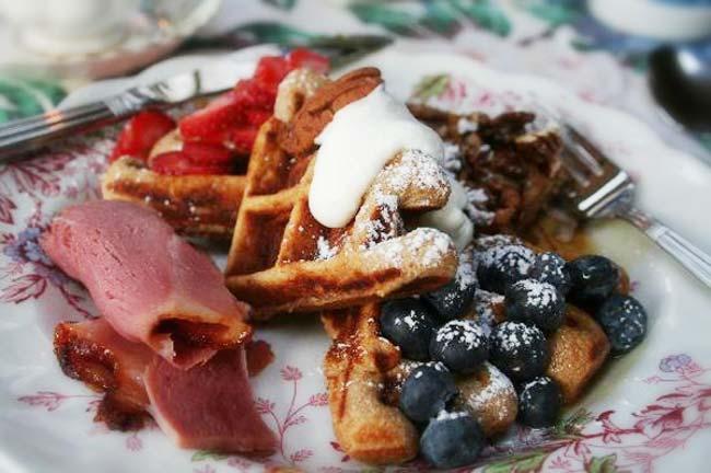 Waffles with berries, cream, and fruit on a floral plate.