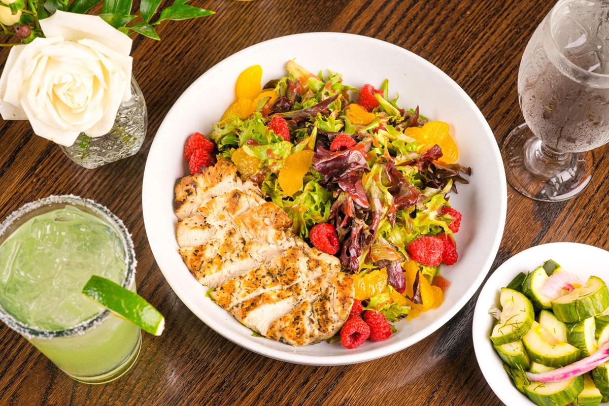 Grilled chicken salad with oranges and raspberries, served with drinks.