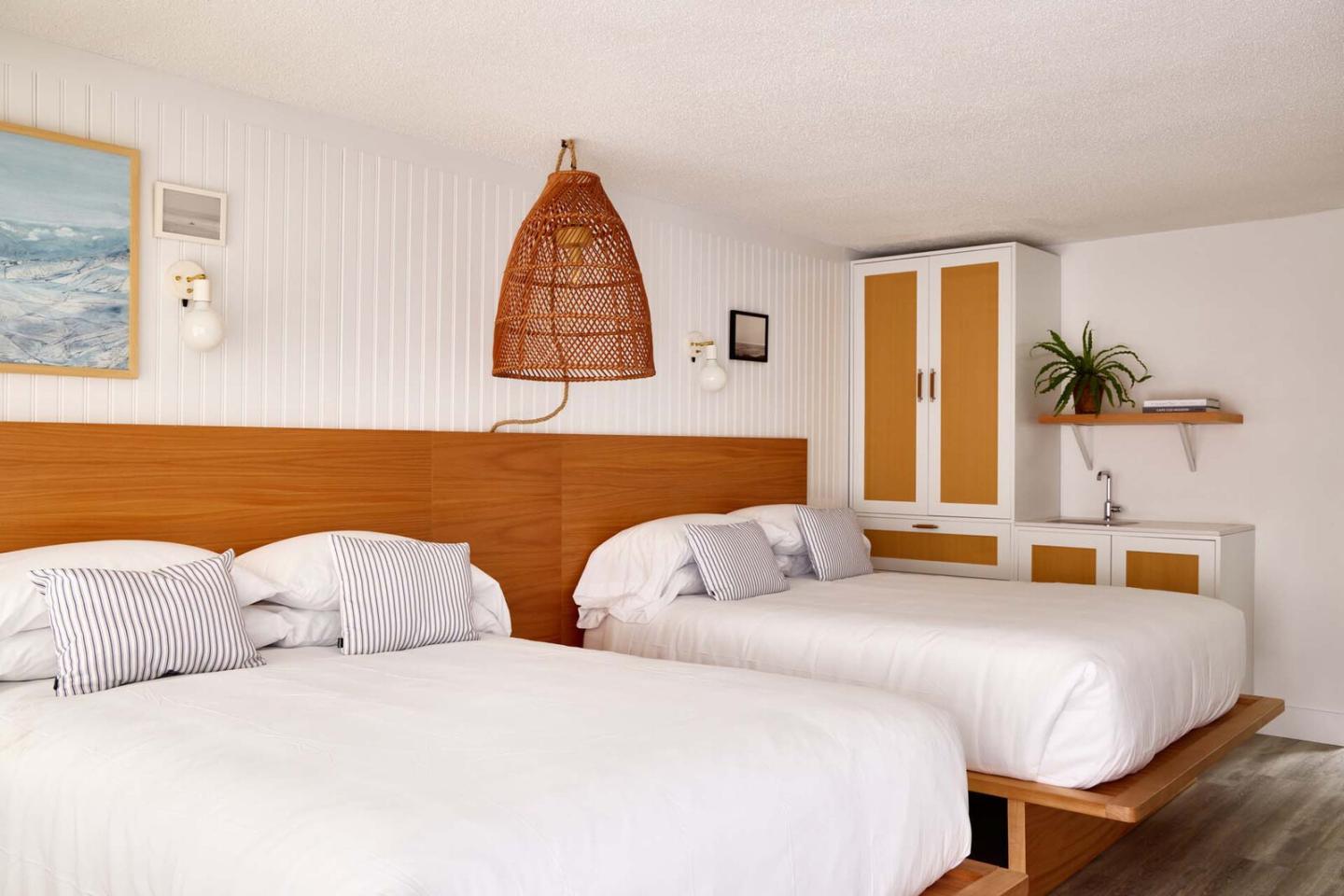 Two beds in a bright, modern hotel room with wooden accents and wall art.