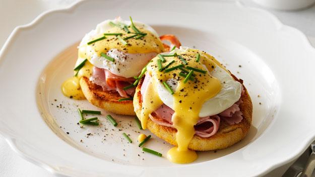 Eggs Benedict topped with hollandaise and chives on a white plate.