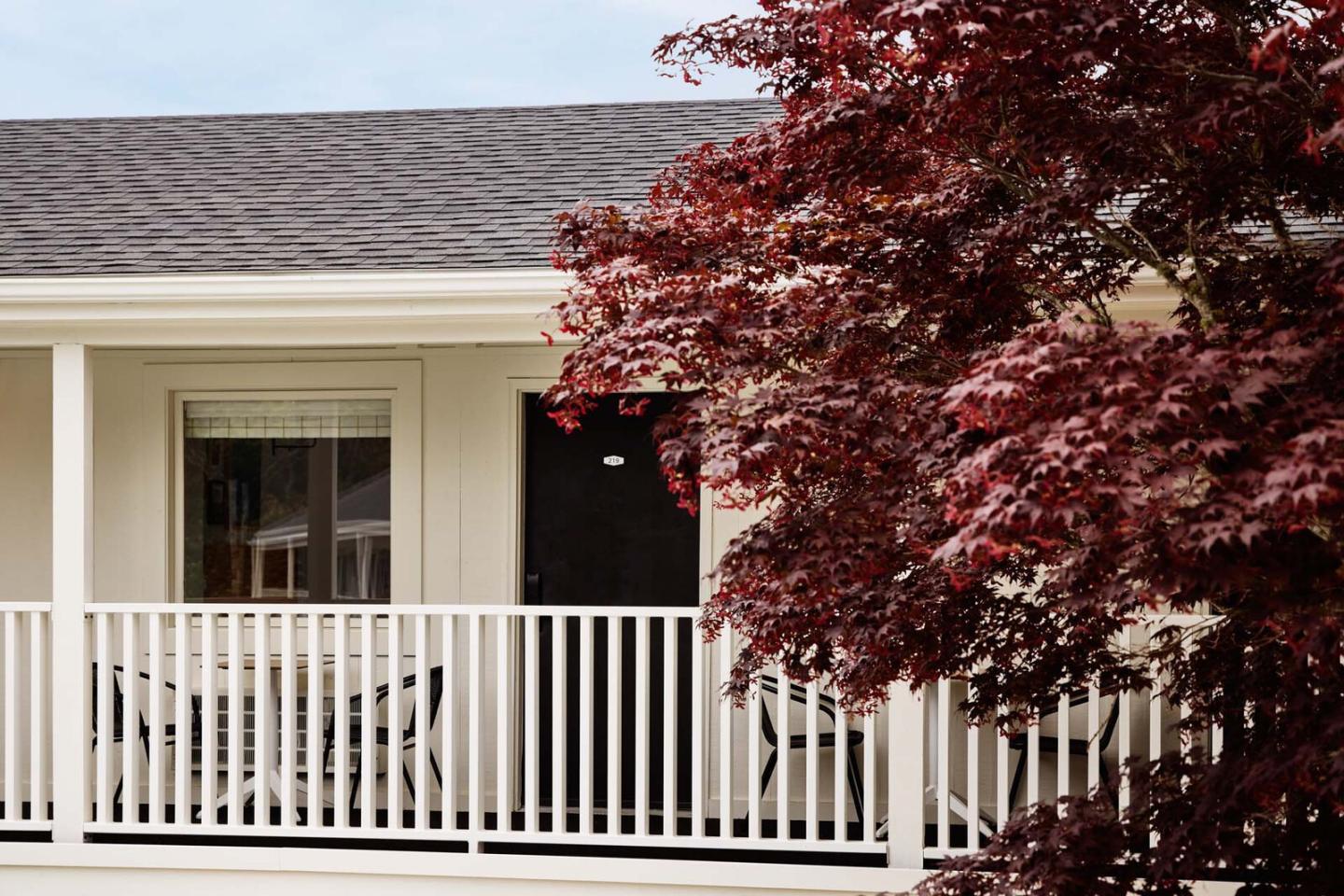 House porch with white railing and a red-leaved tree.