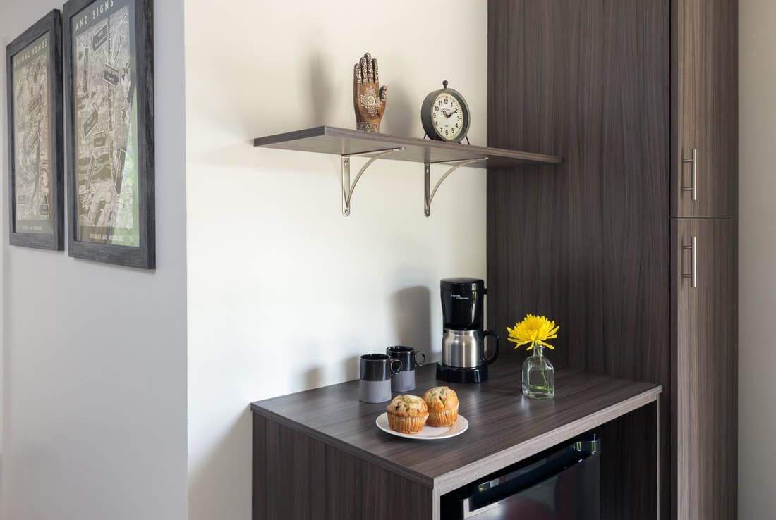 Modern kitchenette with coffee maker, pastries, and flowers on the counter.