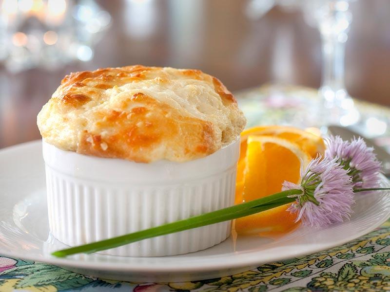 Cheese soufflé in a ramekin with flowers and orange slices.